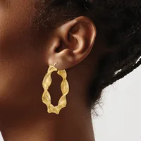 A person wearing a pair of twisted gold hoop earrings with a textured surface, shown from the side profile against a neutral background.