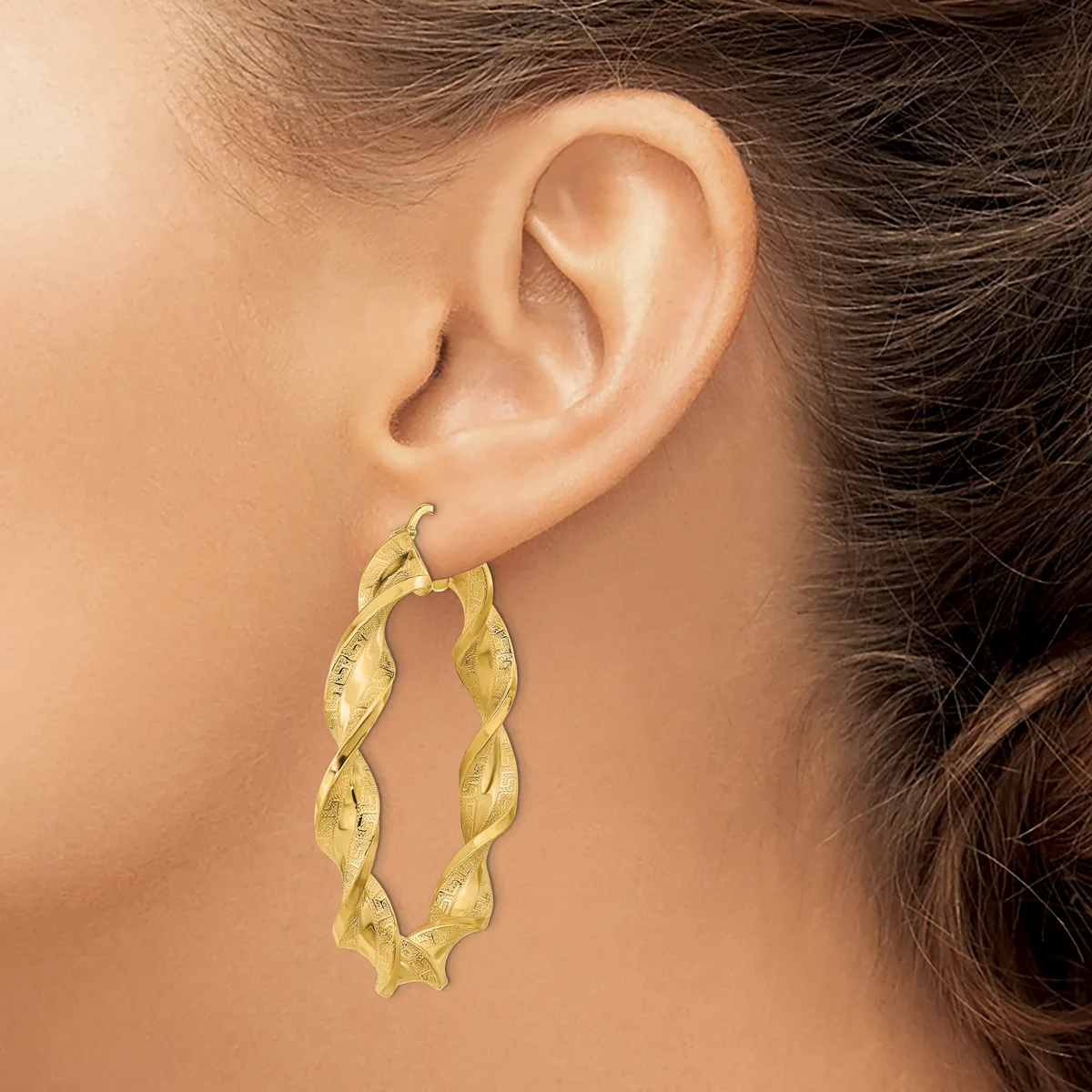 A woman wearing twisted gold hoop earrings with a textured surface, shown from the side profile against her ear.