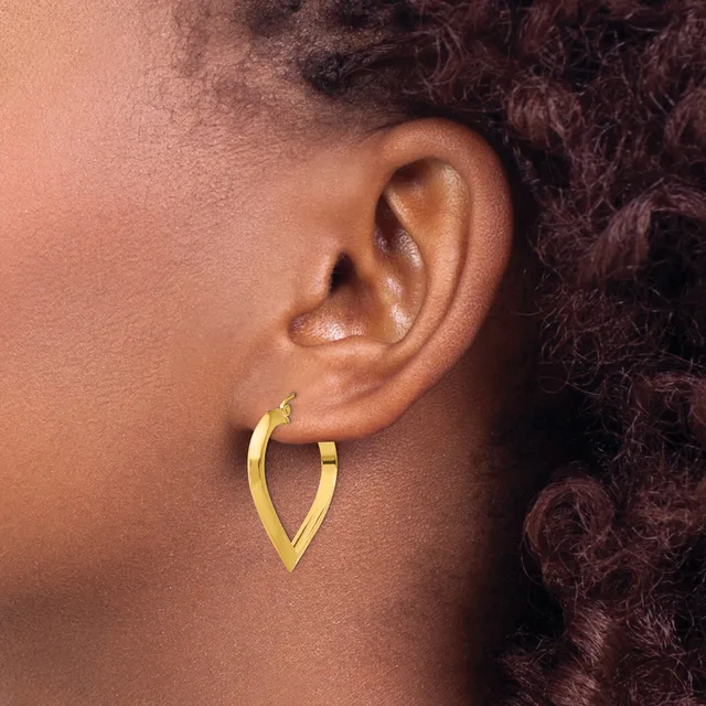 A person wearing a gold-toned V-shaped hoop earring in their pierced earlobe, shown in profile view.