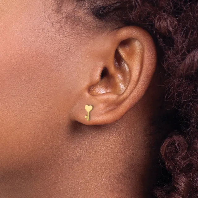 Close-up side view of a person's ear wearing a small gold heart-shaped stud earring.