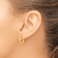 A person wearing a textured gold hoop earring in their pierced earlobe, shown in profile against their shoulder and neck.
