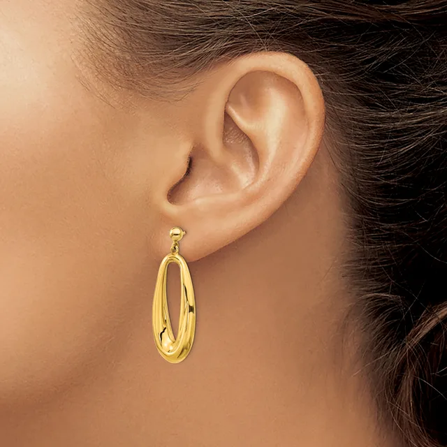 A woman wearing a gold-toned oval hoop earring with a polished finish, shown from the side view of her ear and neck.