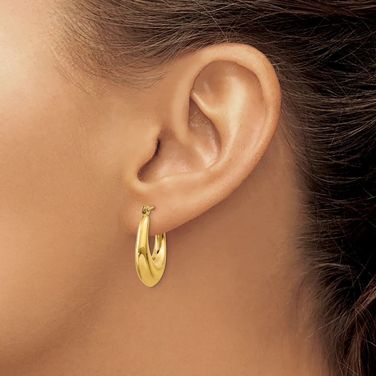 A person wearing a pair of polished gold hoop earrings, shown from the side with dark hair pulled back.