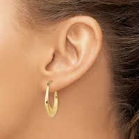 A woman wearing gold hoop earrings with a polished finish, shown from the side profile focusing on the ear and earring detail.