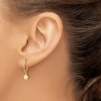 A person wearing a gold hoop earring with a small pale yellow flower charm dangling from it.