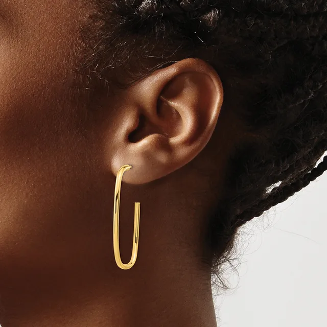 A woman wearing a pair of polished gold hoop earrings with a rounded rectangular shape, shown from the side profile view.