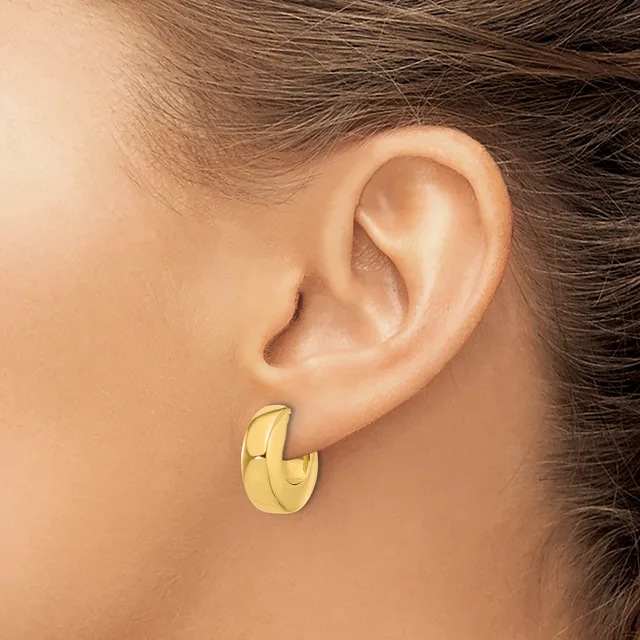 A person wearing a polished gold-colored chunky hoop earring in their pierced earlobe.