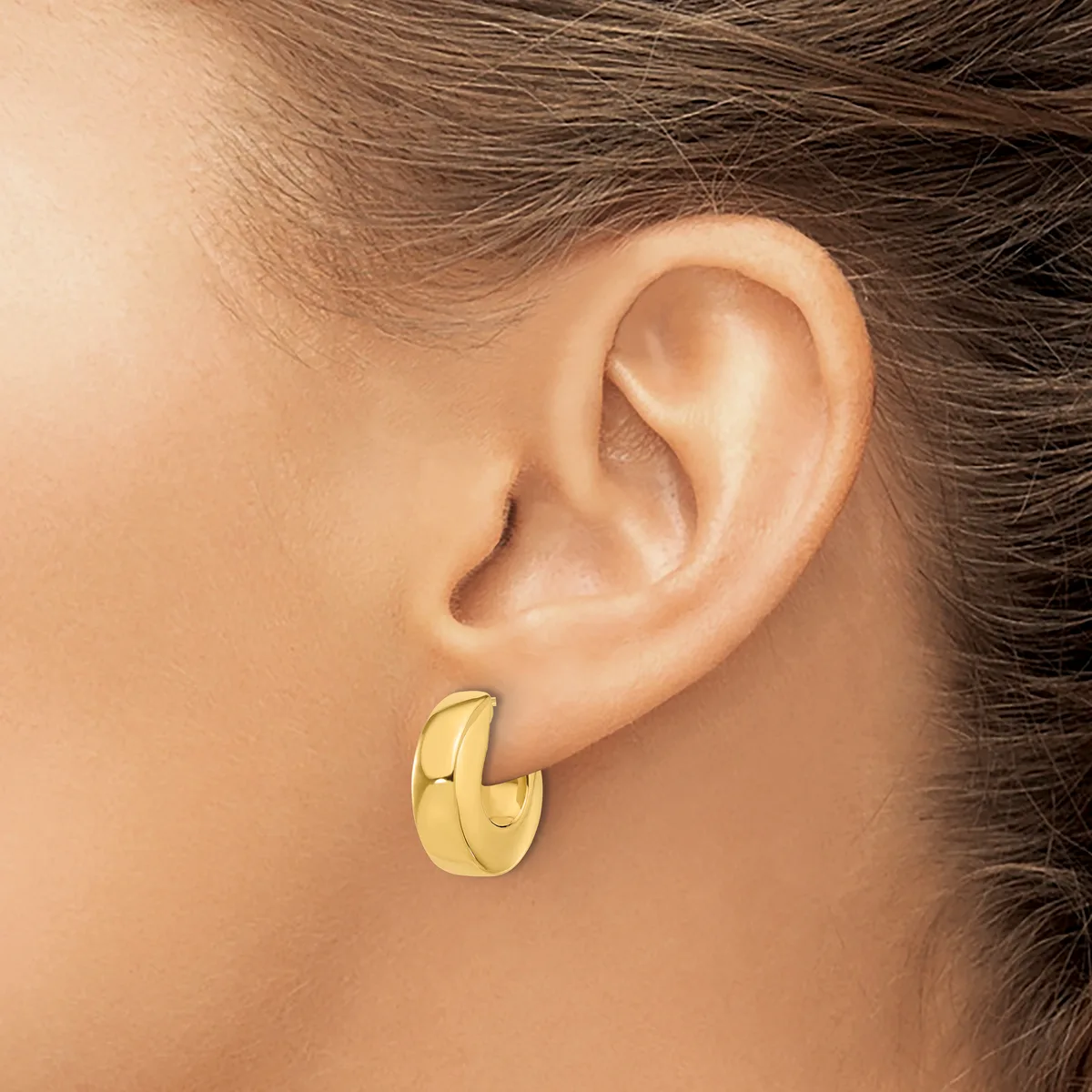 A person wearing a polished gold-colored chunky hoop earring in their pierced earlobe.