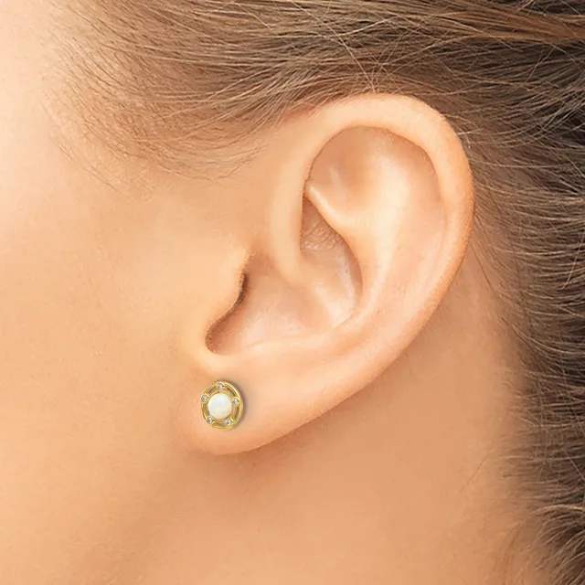 A close-up view of a person's ear wearing a small round stud earring with a pale green stone surrounded by a gold-toned metal bezel.