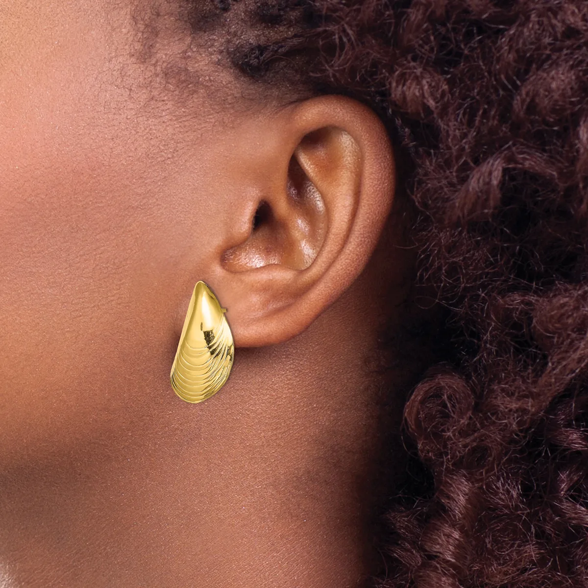 A person wearing a gold teardrop-shaped earring with textured surface detail, shown in profile view against their ear and shoulder.