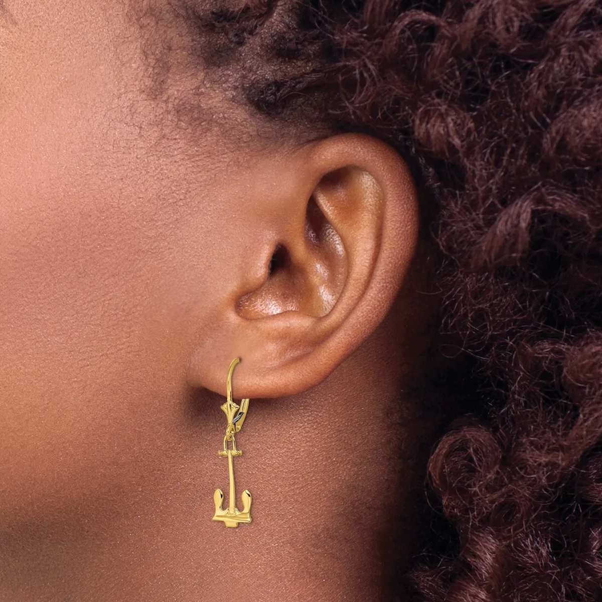 A person wearing a gold-toned anchor charm earring on a hoop, shown from the side profile view.