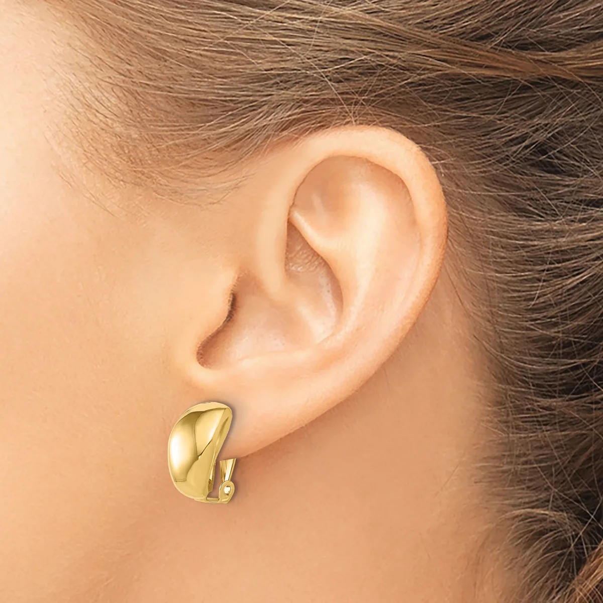 A polished gold-colored curved clip-on earring worn on a person's earlobe, shown from the side view with brown hair visible in the background.