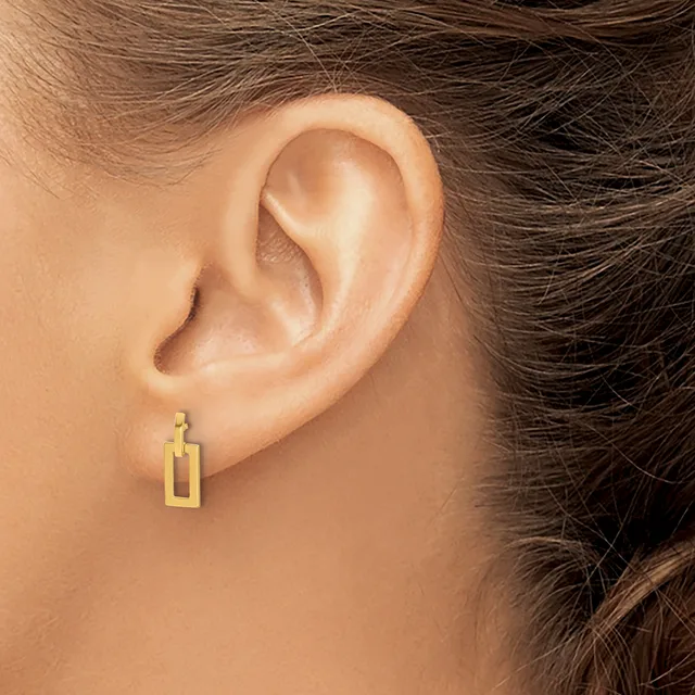 A person wearing a gold rectangular hollow earring with a geometric design, shown from the side view of their ear and neck.