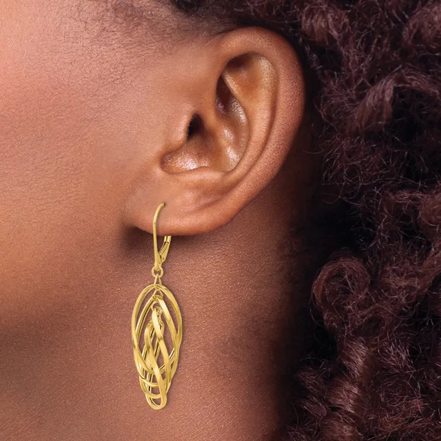 A person wearing a gold-colored dangle earring with an elongated oval design featuring twisted or woven detailing, shown from the side view against their neck and shoulder.