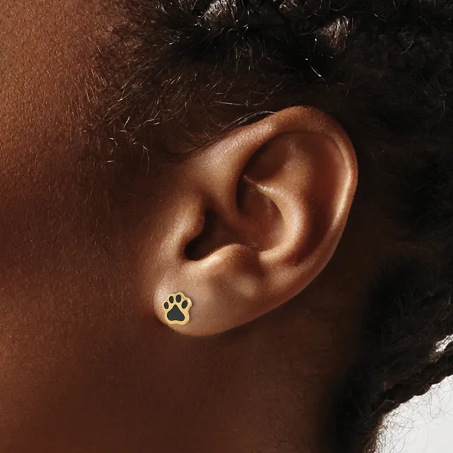 A gold paw print stud earring worn on the earlobe of a person with medium brown skin tone and dark hair.