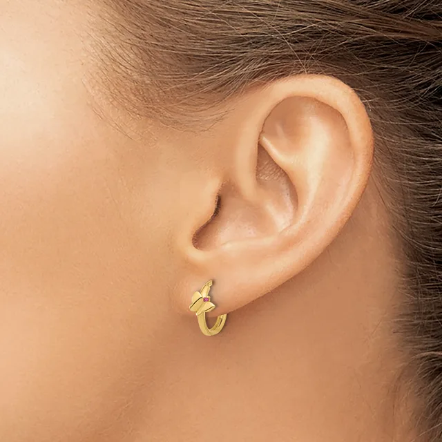 A gold hoop earring with a twisted texture worn in the earlobe of a person with brown hair.