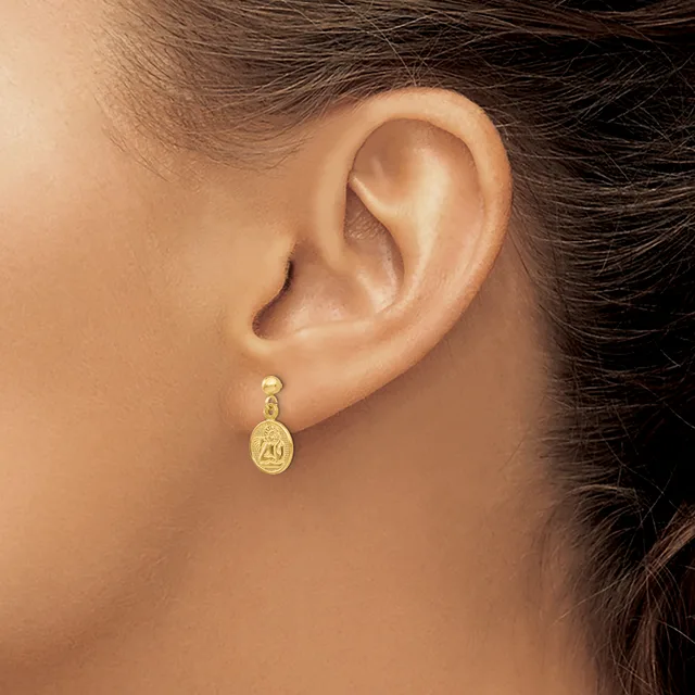 A person wearing a gold drop earring with an oval pendant featuring a small stamped hallmark, shown from the side view of their ear and neck.