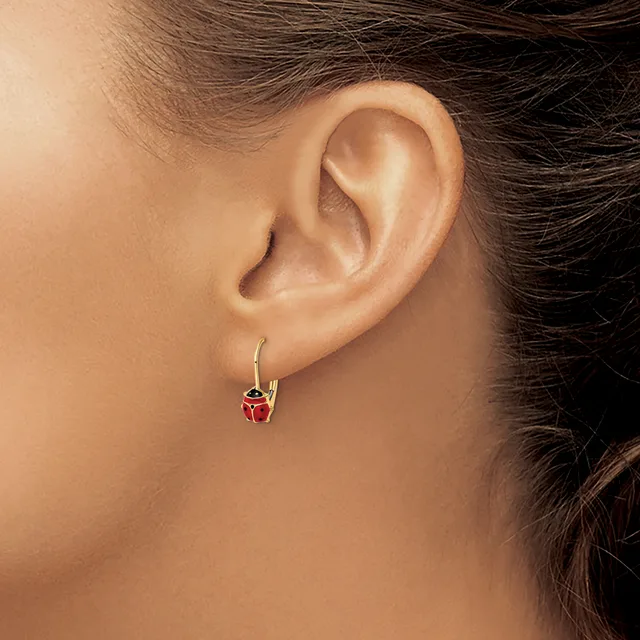 A person wearing a gold hoop earring with a small red enamel ladybug charm hanging from it.