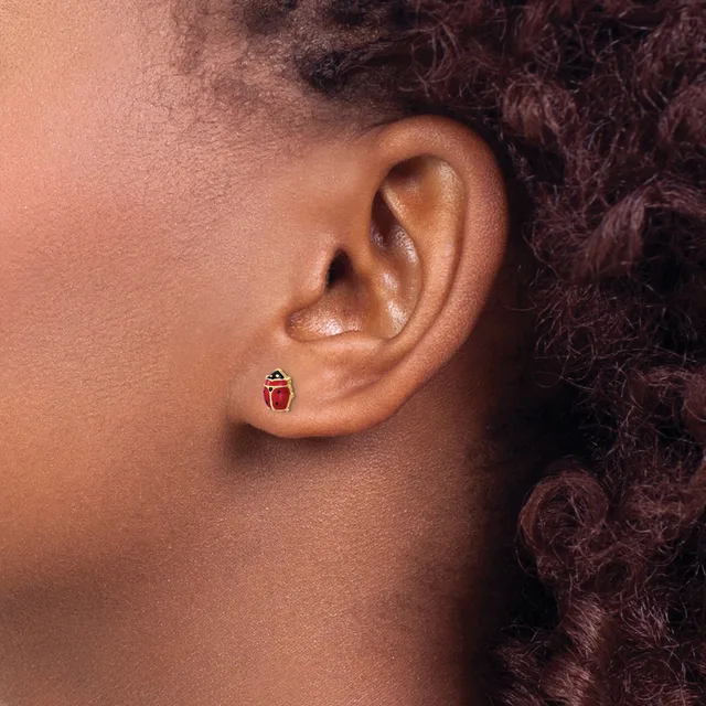 A small red and silver stud earring shaped like a ladybug is worn in the earlobe of a person with dark curly hair.