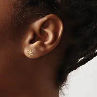 A person wearing a small gold floral stud earring with colorful gemstones in the earlobe.