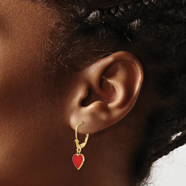 A person wearing a gold hoop earring with a small red enamel heart charm hanging from it.