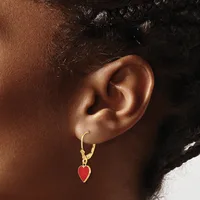 A person wearing a gold hoop earring with a small red enamel heart charm hanging from it.