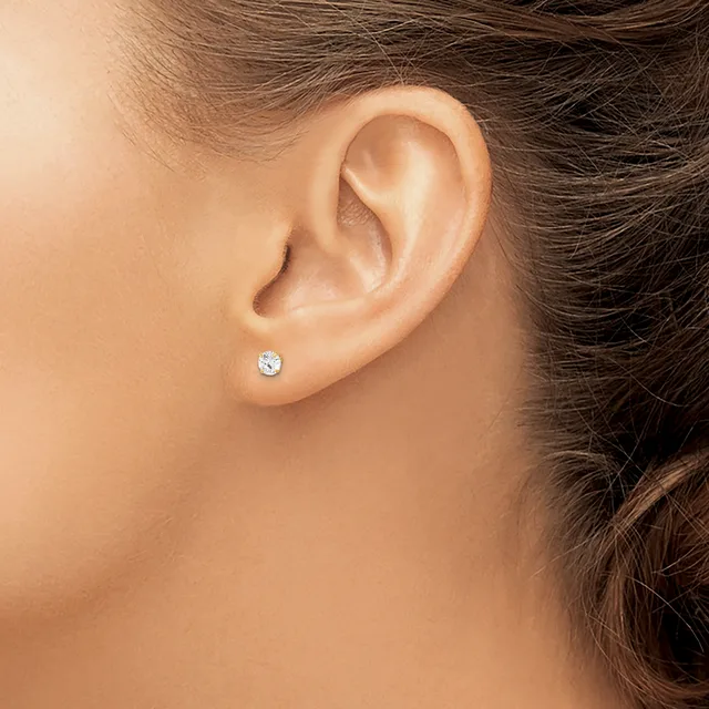 A close-up side view of a person's ear wearing a small round diamond stud earring in a silver setting.