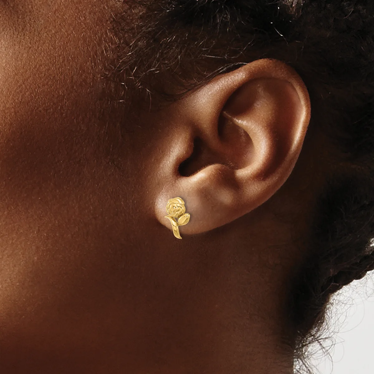 A gold leaf-shaped earring with a textured surface worn in the earlobe of a person with medium brown skin tone.