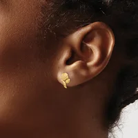 A gold leaf-shaped earring with a textured surface worn in the earlobe of a person with medium brown skin tone.