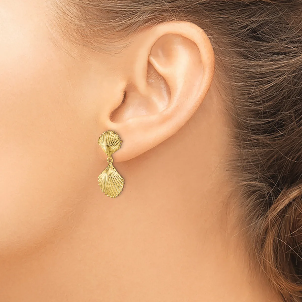 A person wearing gold shell-shaped drop earrings with textured surfaces, shown from the side profile of their ear and neck.