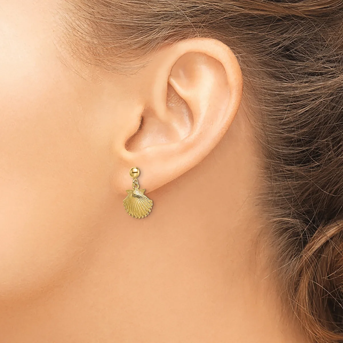 A woman wearing a gold shell-shaped dangle earring on a post with a ball backing, shown from the side view of her ear.