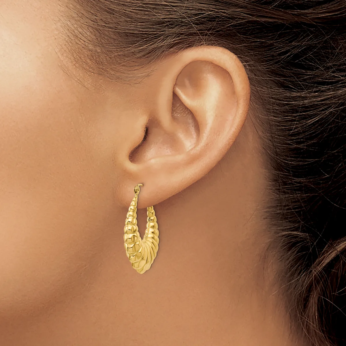 A woman wearing gold textured hoop earrings with a ridged surface pattern, shown from the side view of her face and ear.