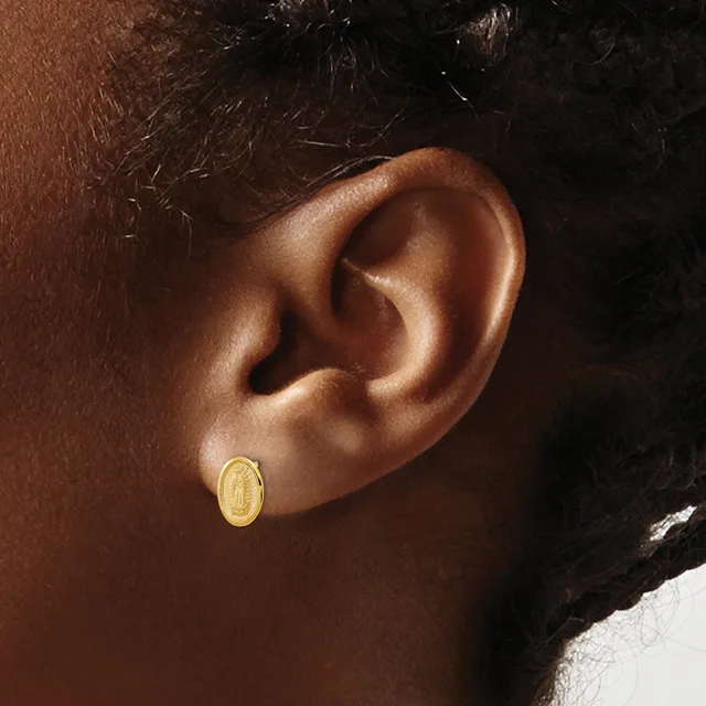 A close-up of a person's ear wearing a small oval gold stud earring with a textured surface.