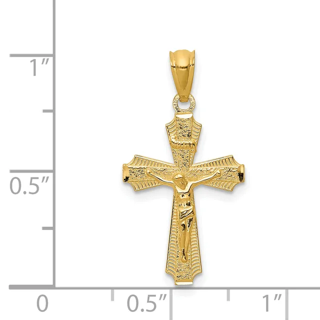 A gold crucifix pendant with textured detailing and a corpus figure, shown next to a ruler indicating approximately one inch in height.