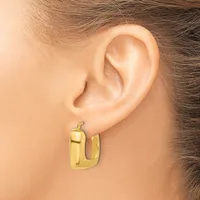 A person wearing a gold-toned chunky rectangular hoop earring with a polished finish, shown on their earlobe.