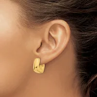 A person wearing a polished gold-toned rectangular hoop earring with a curved, chunky design on their earlobe.