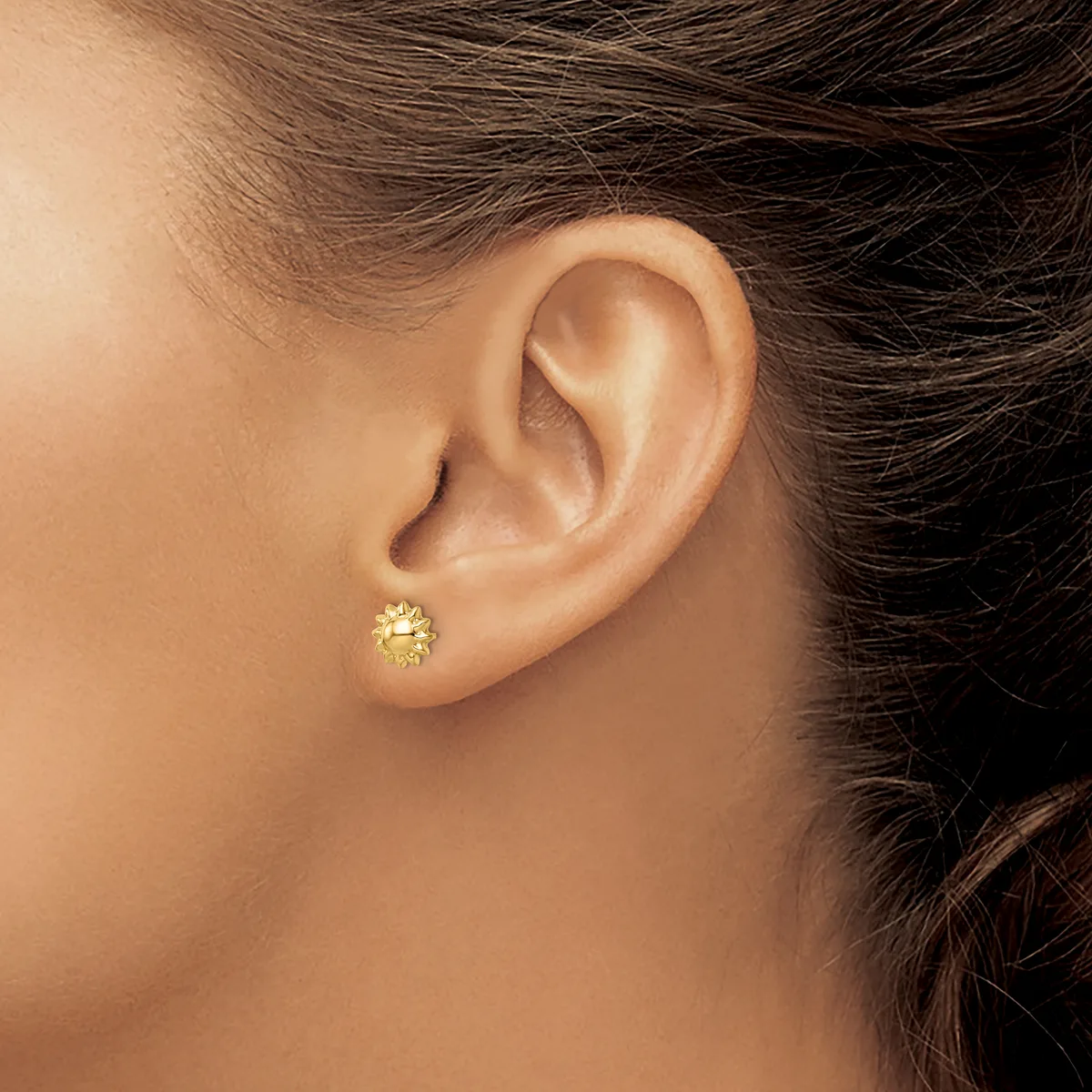 A close-up view of a person's ear wearing a small gold stud earring with a textured, bumpy surface.
