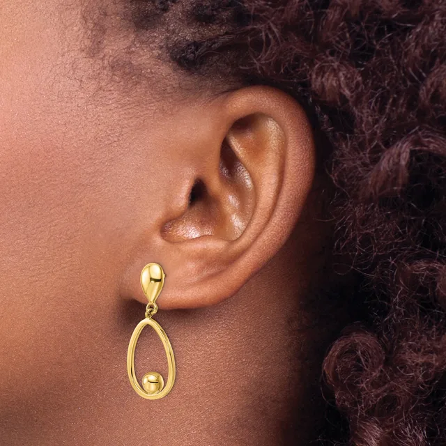 A person wearing a gold teardrop-shaped dangle earring with a spherical stud post, shown from the side view of their ear.