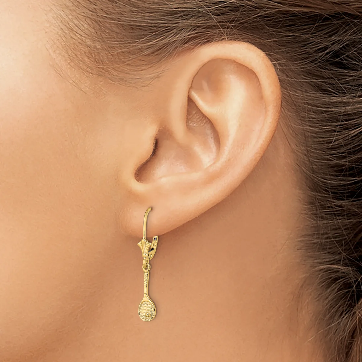 A gold teardrop dangle earring with textured detailing hangs from a gold hook on a model's earlobe.