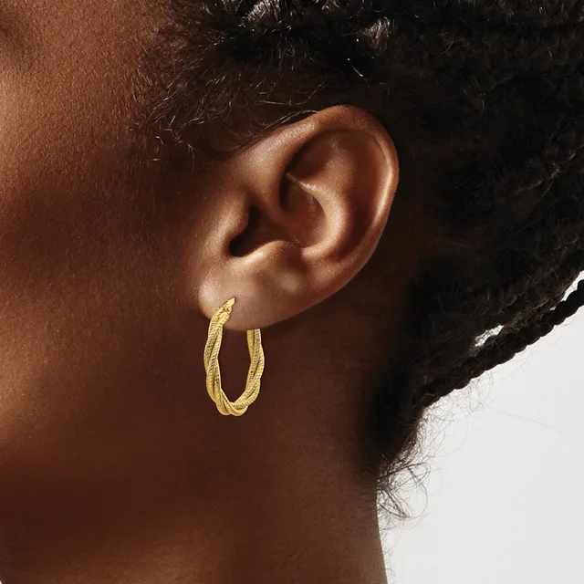 A person wearing textured gold-colored hoop earrings, shown in profile from the side of their face and neck.