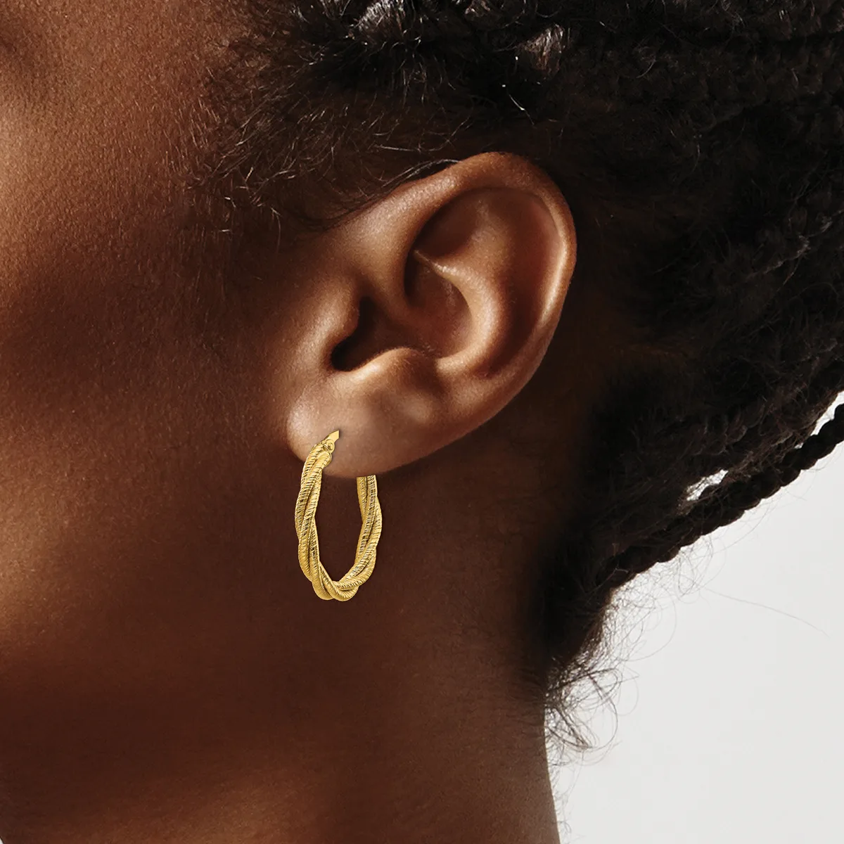A person wearing textured gold-colored hoop earrings, shown in profile from the side of their face and neck.