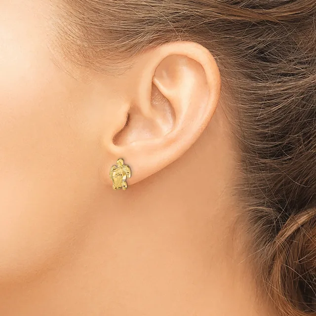 A person wearing a small gold turtle-shaped earring with a textured finish on their earlobe.