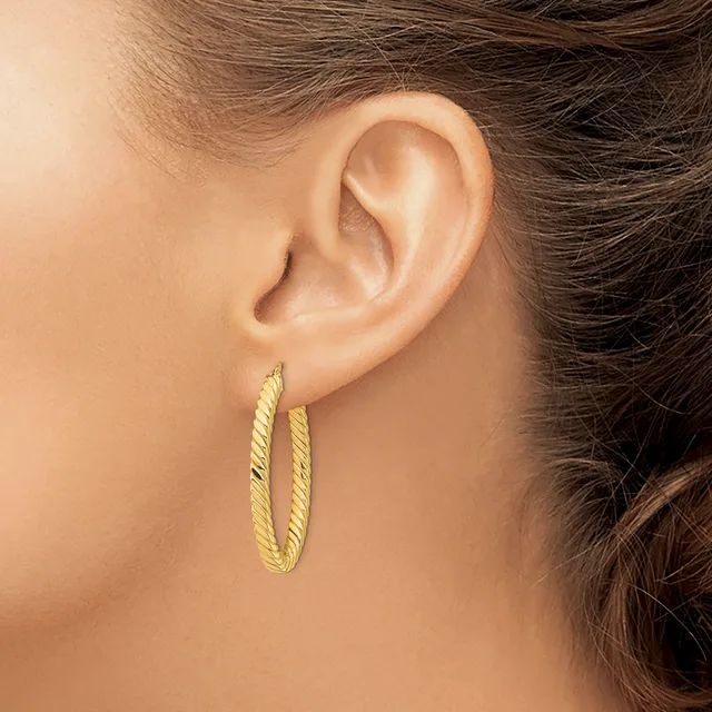 A woman wearing textured gold hoop earrings with a twisted finish, shown from the side profile of her ear and neck.