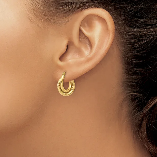 A woman wearing textured gold hoop earrings, shown from the side with her ear and dark hair visible.