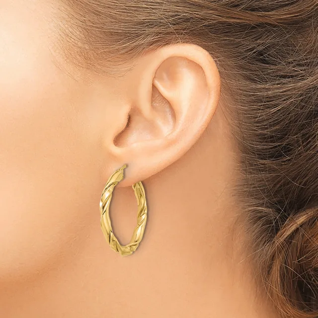 A woman wearing a pair of twisted gold hoop earrings with a textured surface, shown from the side profile of her head and ear.