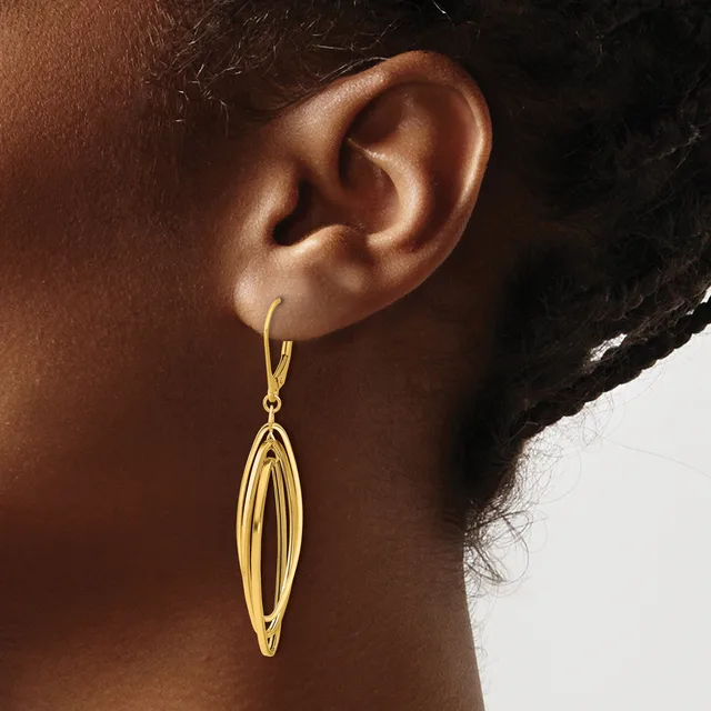 A gold-toned elongated oval drop earring with parallel ridged detailing hangs from a hook on a person's earlobe.