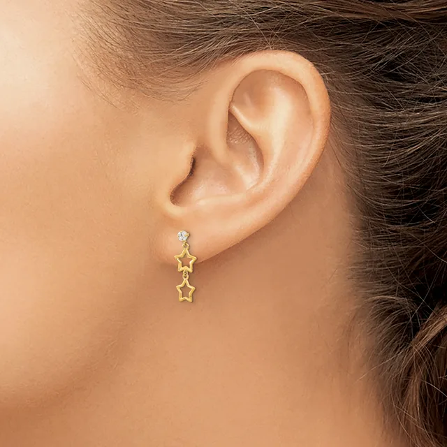 A person wearing gold star-shaped drop earrings with a diamond stud, shown from the side view of their ear and neck.