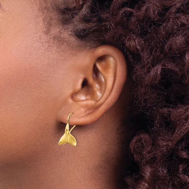 A person wearing a small gold-colored teardrop-shaped earring with a hook closure, shown from the side profile of their ear.