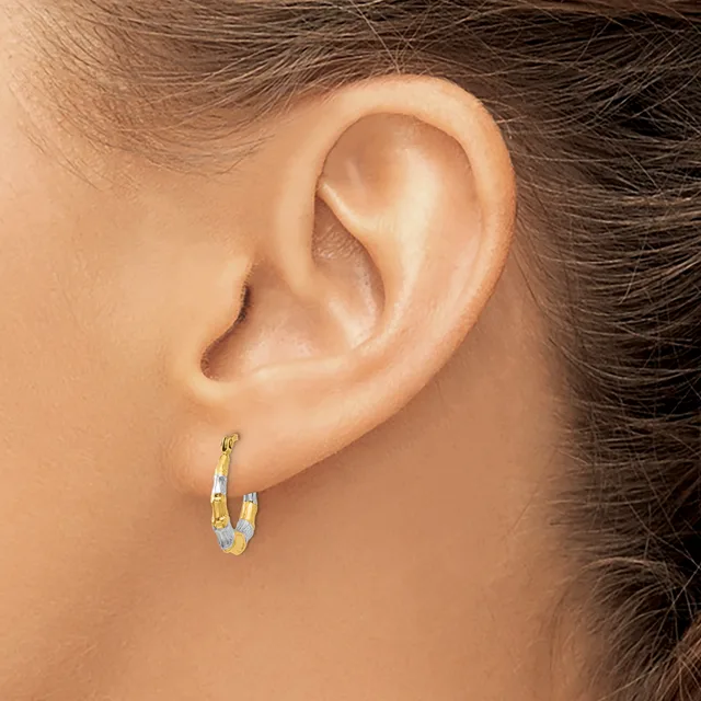 A person wearing small gold and silver two-tone hoop earrings with a textured finish, shown from the side view of their ear and neck.
