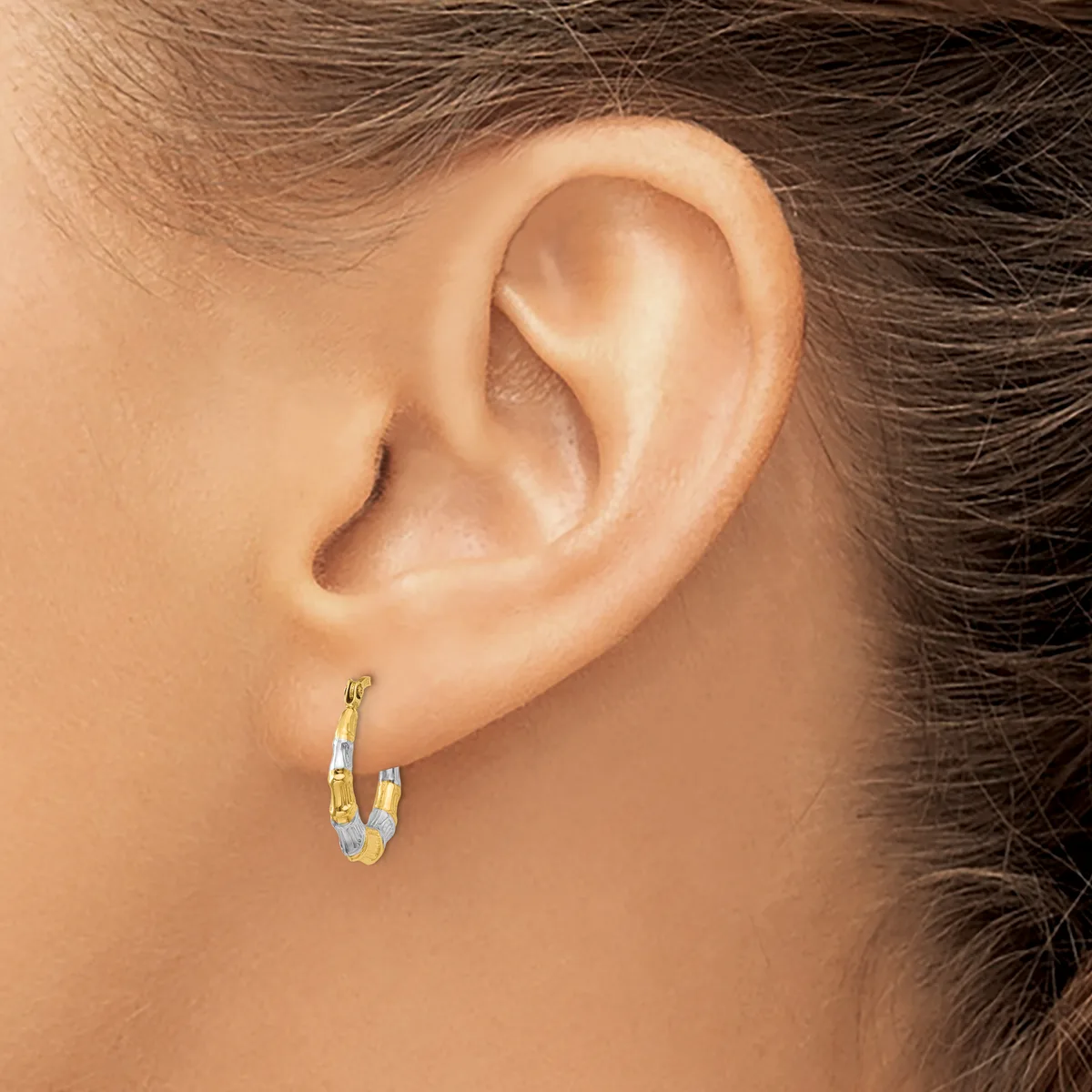 A person wearing small gold and silver two-tone hoop earrings with a textured finish, shown from the side view of their ear and neck.